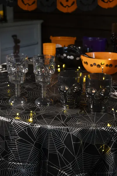 Halloween-teemainen pöytäkattaus, jossa on pääkallokuvioisia laseja, hämähäkinseittikuvioinen pöytäliina ja oransseja tarjoiluastioita.