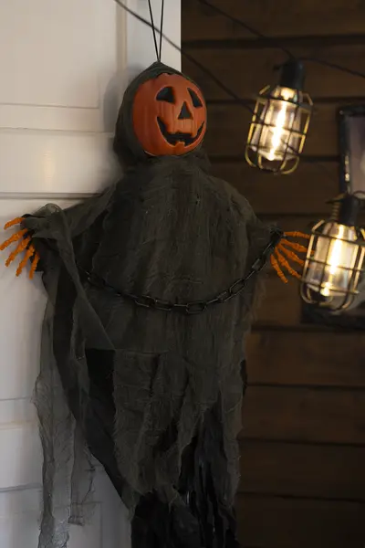 Kurpitsapäinen riippuva halloween-koriste seinällä ulkovalojen vieressä.