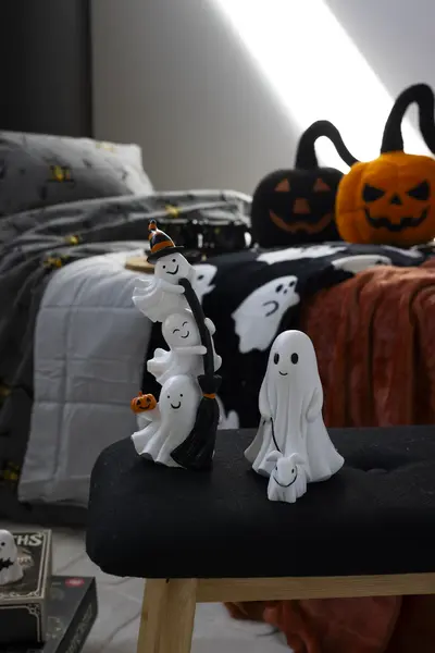 Kaksi valkoista haamukoristetta tuolilla makuuhuoneessa. Taustalla näkyy sängyllä halloween-aiheisia tekstiilejä ja kurpitsatyynyjä.