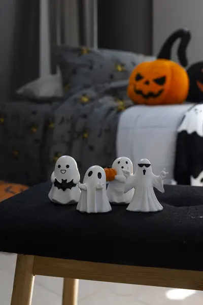 Pienet haamuhahmot somisteena tuolilla, taustalla halloween-aiheinen päiväpeitto ja kurpitsakoriste.