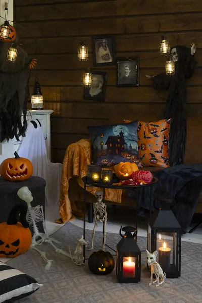 Halloween-teemainen olohuoneen sisustus, jossa on kurpitsoita, lyhtyjä, koristevaloja, luurankokoristeita ja tummasävyisiä tekstiilejä.