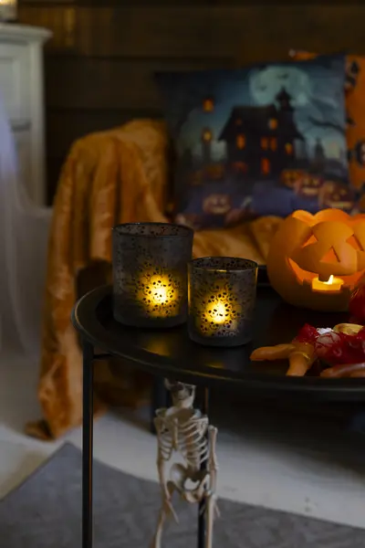 Tunnelmallinen halloween-asetelma sohvapöydällä, jossa palavat lyhdyt, kurpitsalyhty ja pieni luurankokoriste.