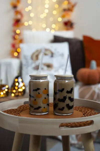 Lepakkokuvioidut pillimukit pienellä sivupöydällä osana syksyistä ja halloween-henkistä sisustusta.