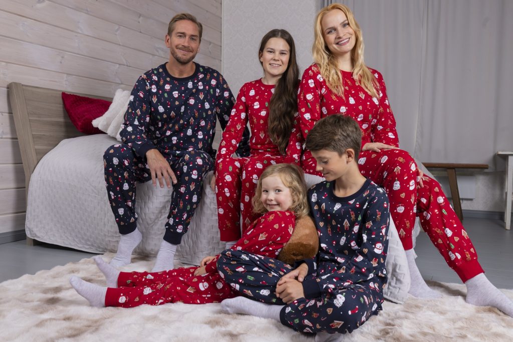 Perhe yhteensopivissa jouluisissa pyjamissa makuuhuoneessa. Punaiset ja tummansiniset kuosit tuovat tunnelmaa joulun yhdessäoloon.