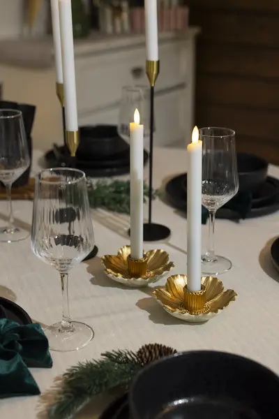 Jouluisesti katettu ruokapöytä, jossa kynttilänjalat, lasit ja havukoristeet viimeistelevät kattauksen.