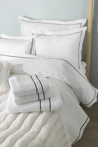 Pedattu valkoinen hotellityylinen vuode, yhteensopivat koristetyynyt ja taitellut pyyhkeet tummansinisillä yksityiskohdilla.