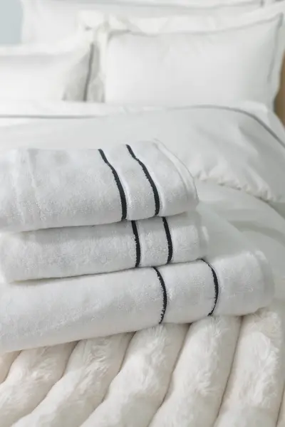 Valkoiset hotellityyliset pyyhkeet tummansinisillä reunuksilla pedatun vuoteen päällä.